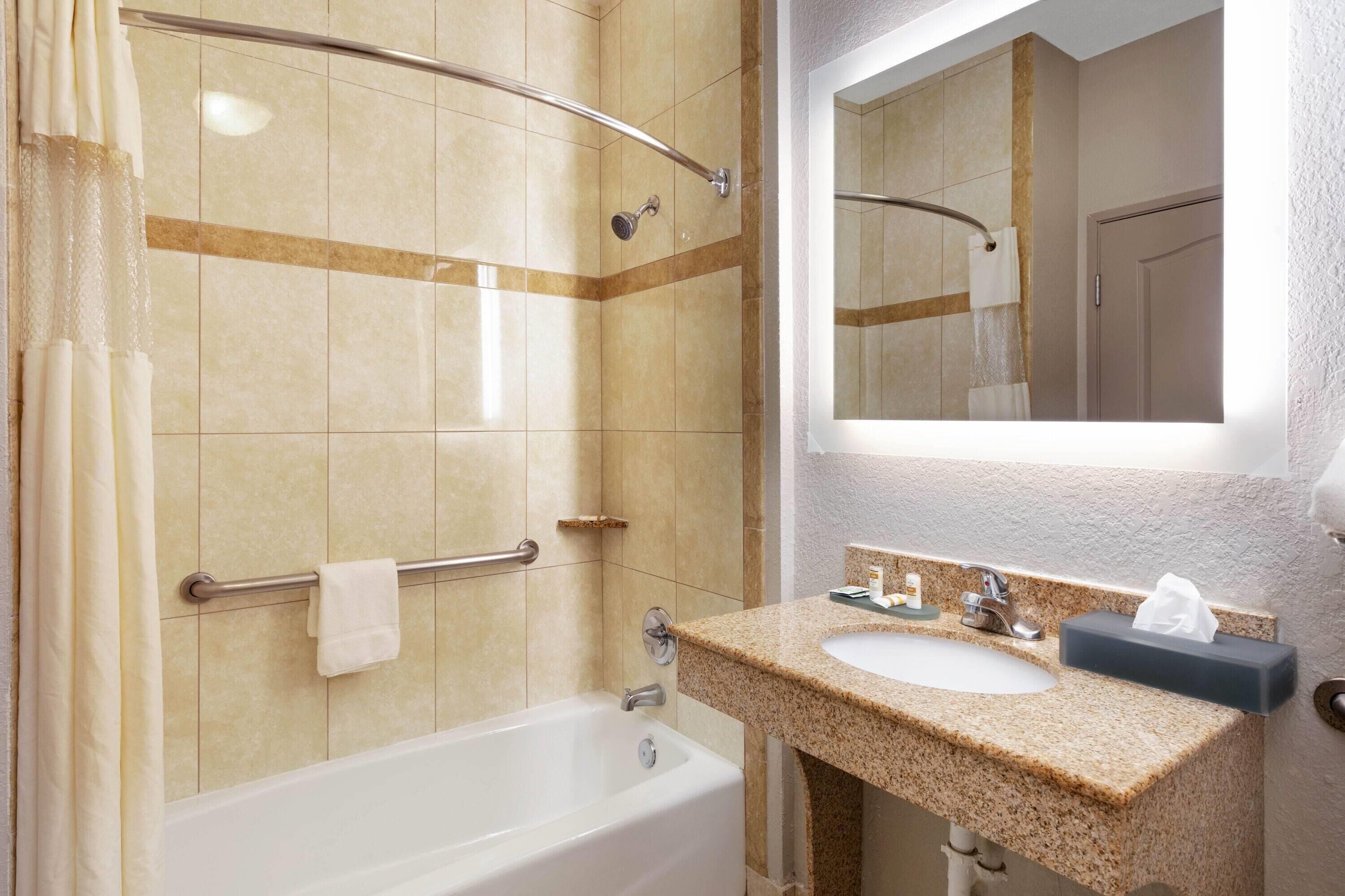 Un baño con bañera, ducha con mampara de vidrio, lavabo con espejo arriba y un perchero para toallas.