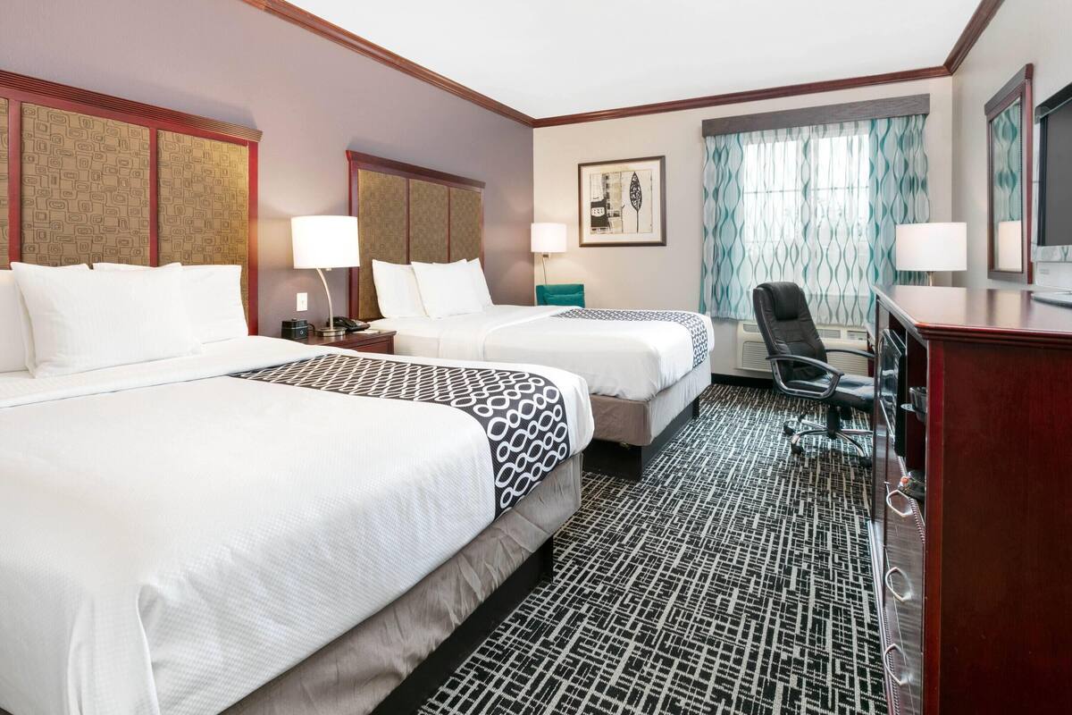A hotel room with two beds, a desk, a chair, and a television.