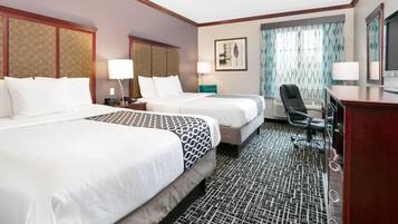 A hotel room with two beds, a desk, a chair, and a television.