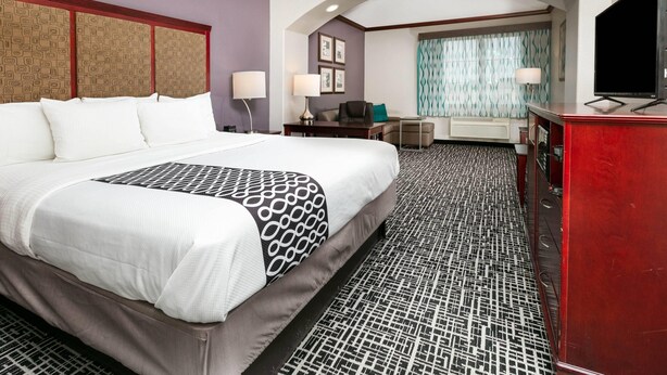 Ein Hotelzimmer mit einem großen Bett, einem Schreibtisch, einem Sessel, einem Fernseher und einer kleinen Sitzecke mit einer Couch und einem Tisch.