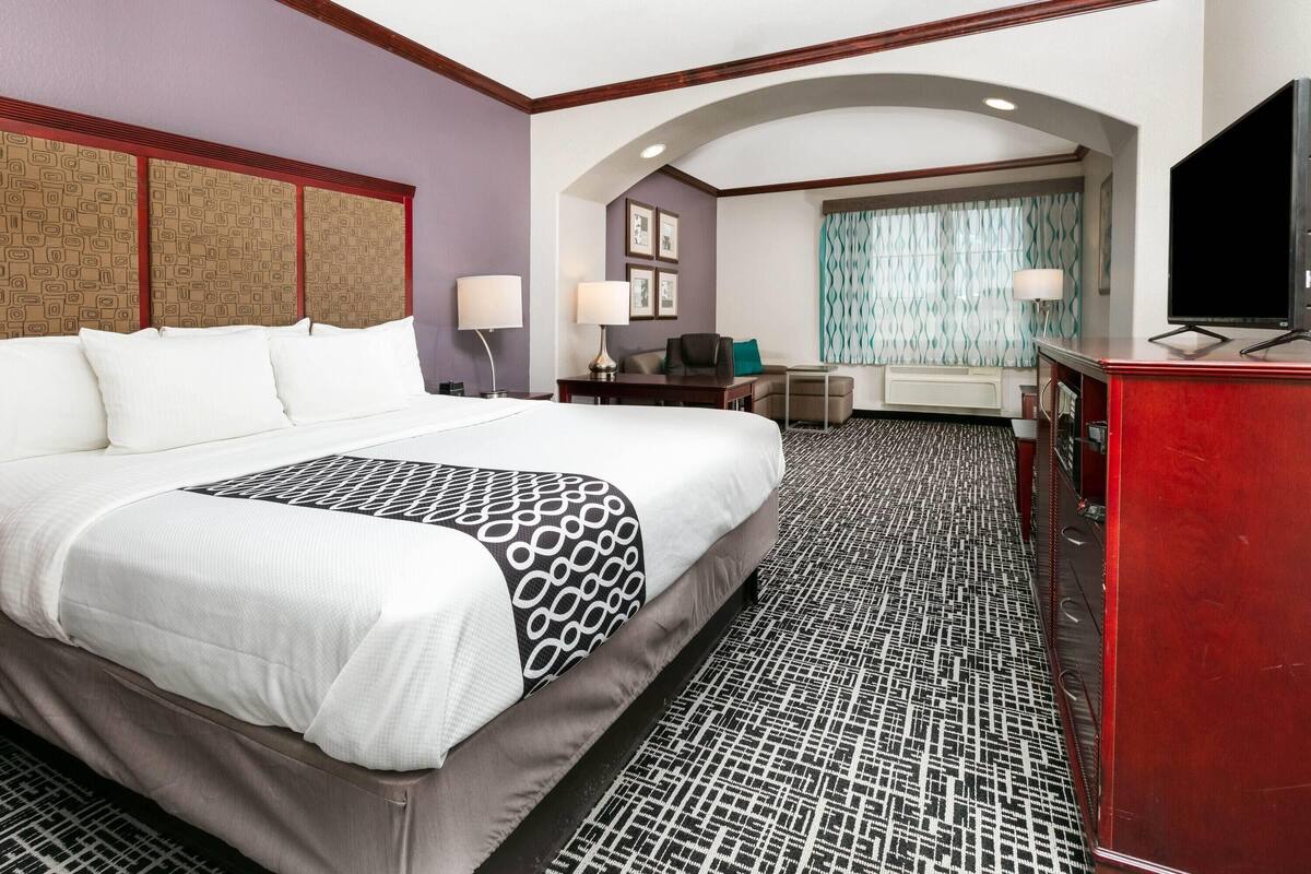 A hotel room with a large bed, a desk, a chair, a TV, and a small seating area with a couch and a table.