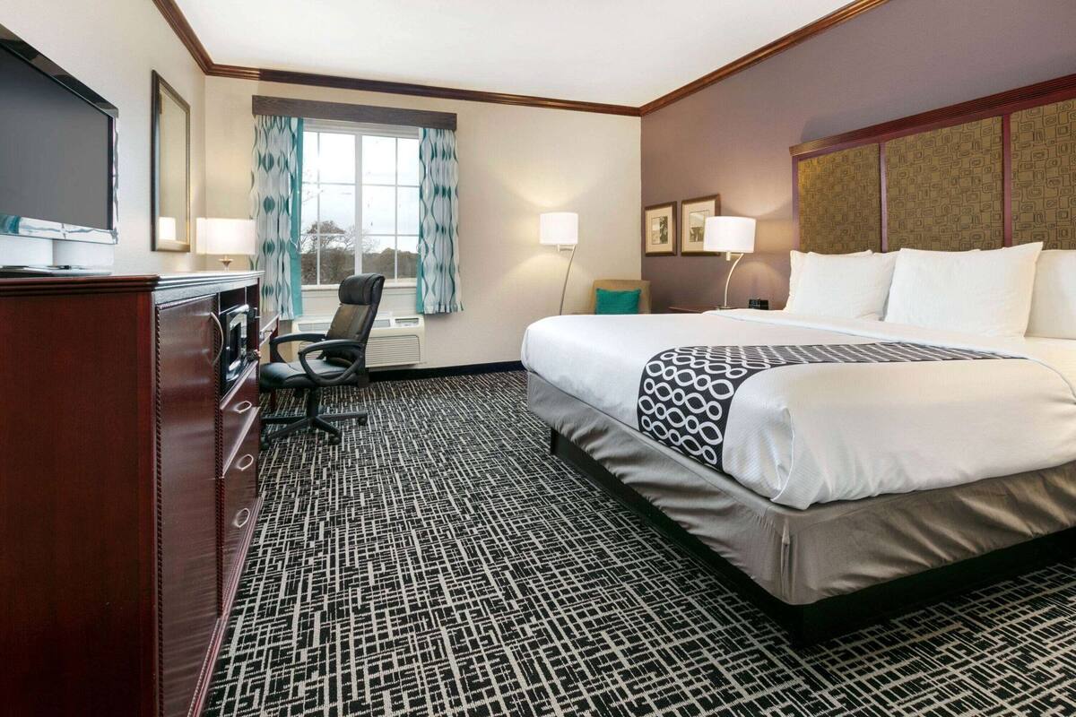 A hotel room with a bed, desk, chair, TV, and window with curtains.