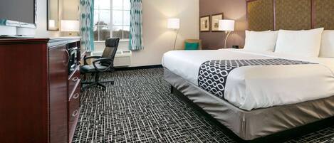 A hotel room with a large bed, a desk with a chair, a television, and a window with curtains.