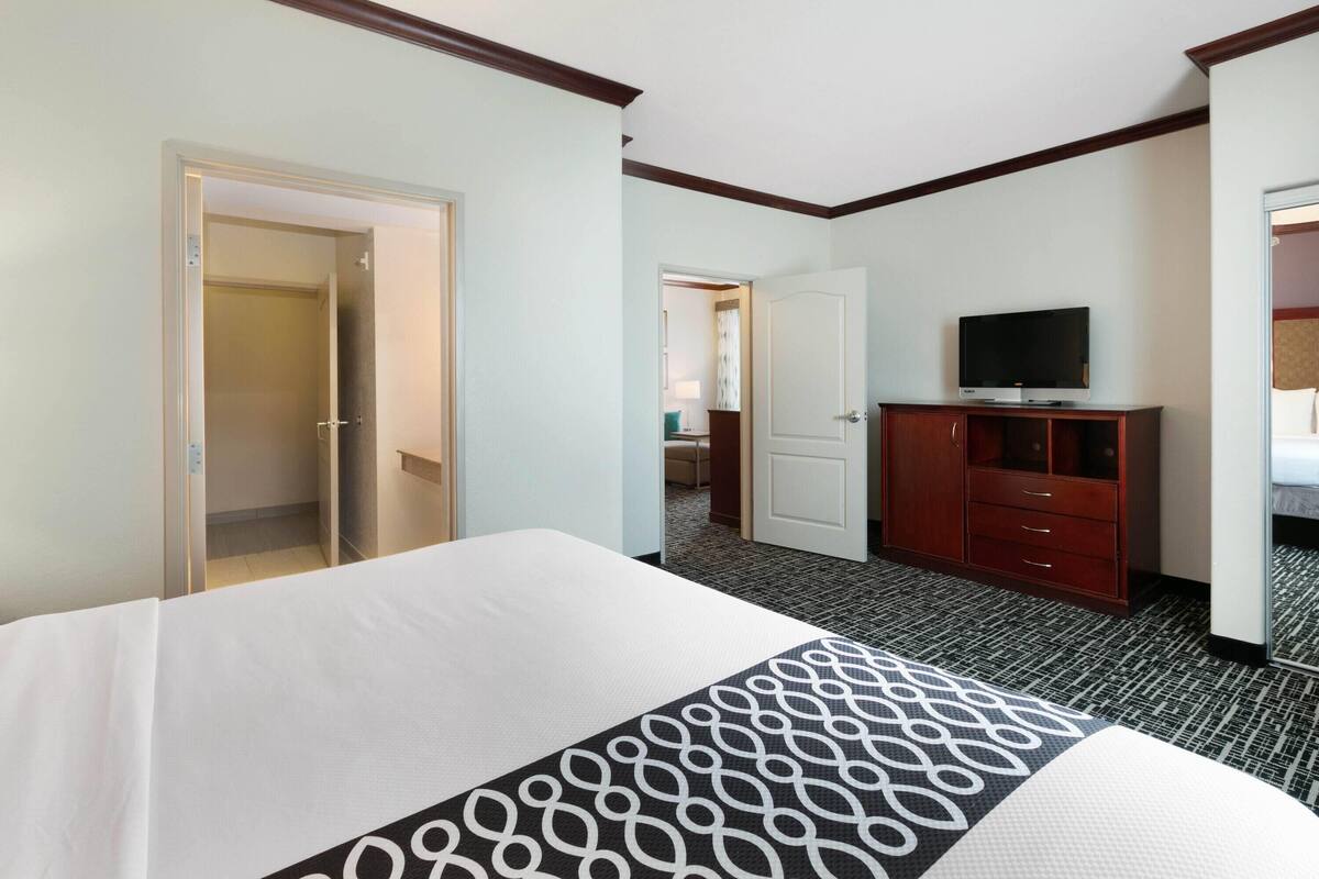 A hotel room with a bed, a television on a wooden cabinet, and a door leading to another room.