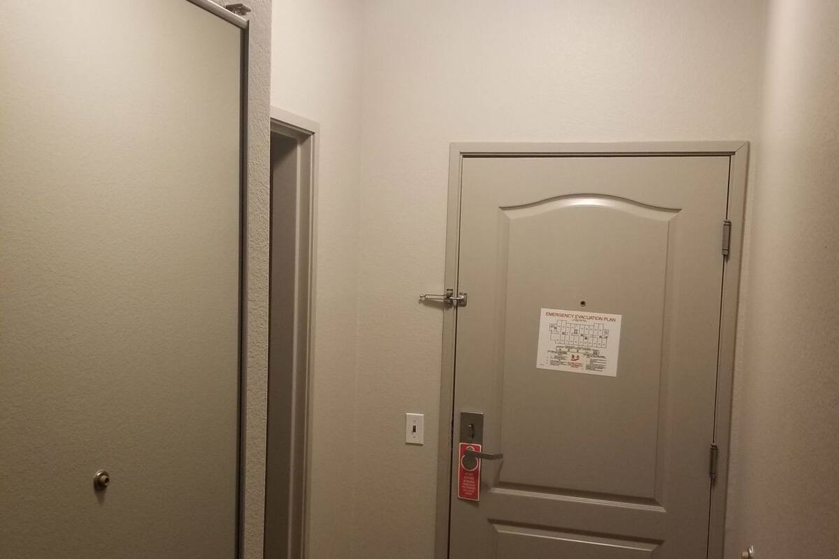A hallway with a door that has an emergency evacuation plan posted on it, a fire alarm, and a ceiling light.