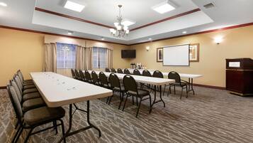 A conference room with a long table, chairs, a projector screen, and a podium.