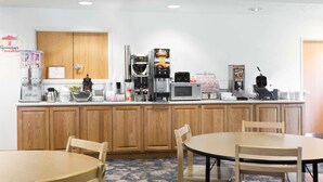 A hotel room with a wooden cabinet, a microwave, a coffee machine, and a dining table with chairs. - Super 8 by Wyndham Alma (Alma)