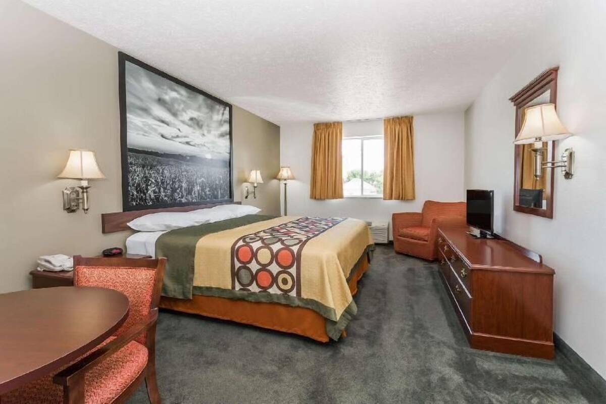 A hotel room with a bed, a desk, a chair, a TV, and a large painting on the wall.