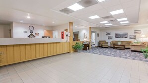 A reception area with a wooden reception desk, tiled flooring, and several seating areas with sofas and chairs. - Super 8 by Wyndham Alma (Alma)