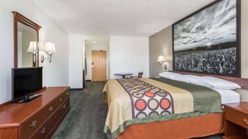 A hotel room with a bed, a TV on a dresser, a desk, and a large painting on the wall.