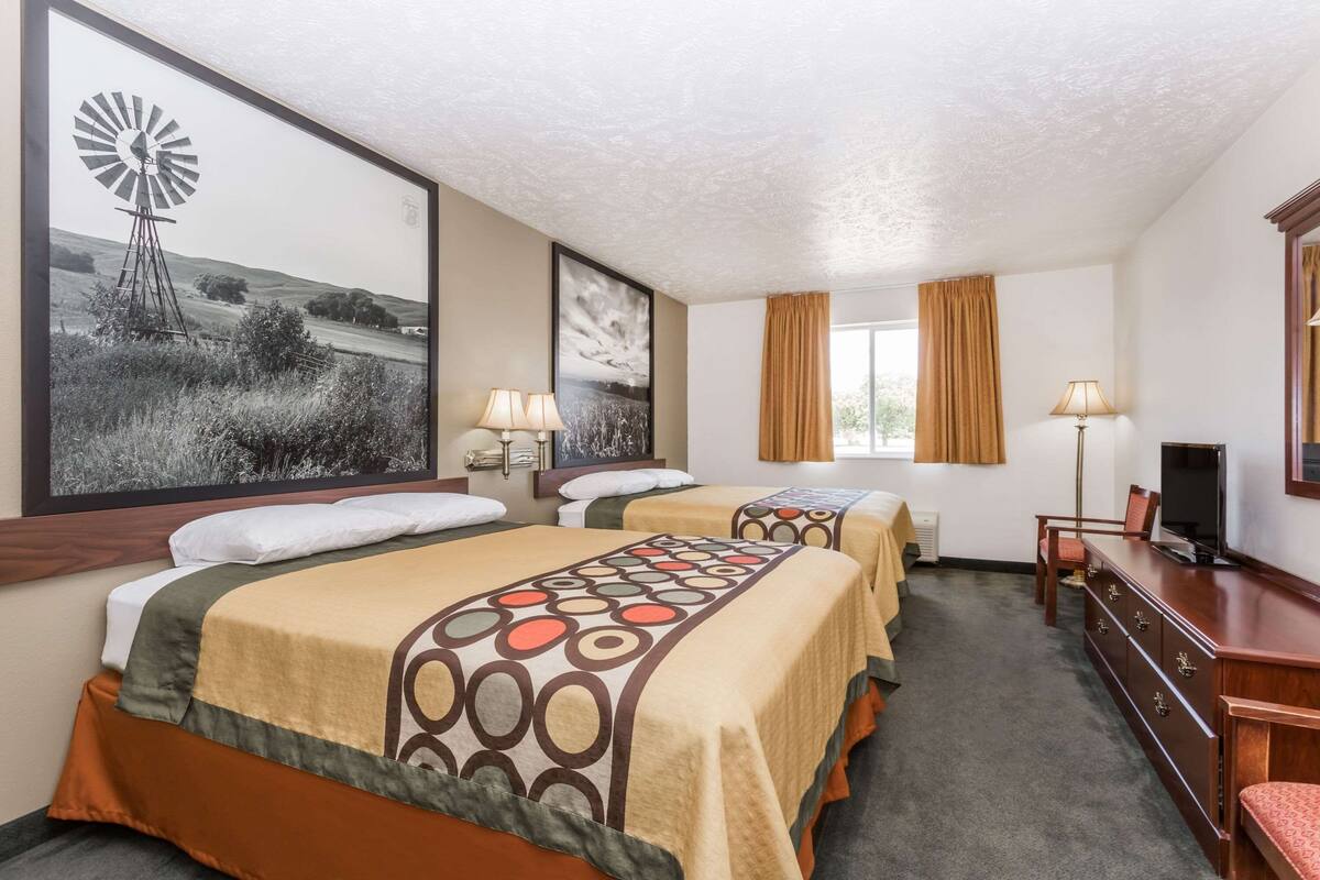 A hotel room with two beds, a television, a dresser, and a large window with curtains.
