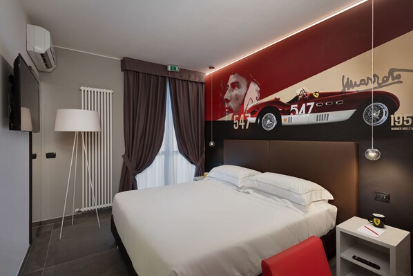 Una habitación de hotel moderna con una cama grande, una silla roja, una mesita de noche con un control remoto, una lámpara de pared y un gran ventanal con cortinas.