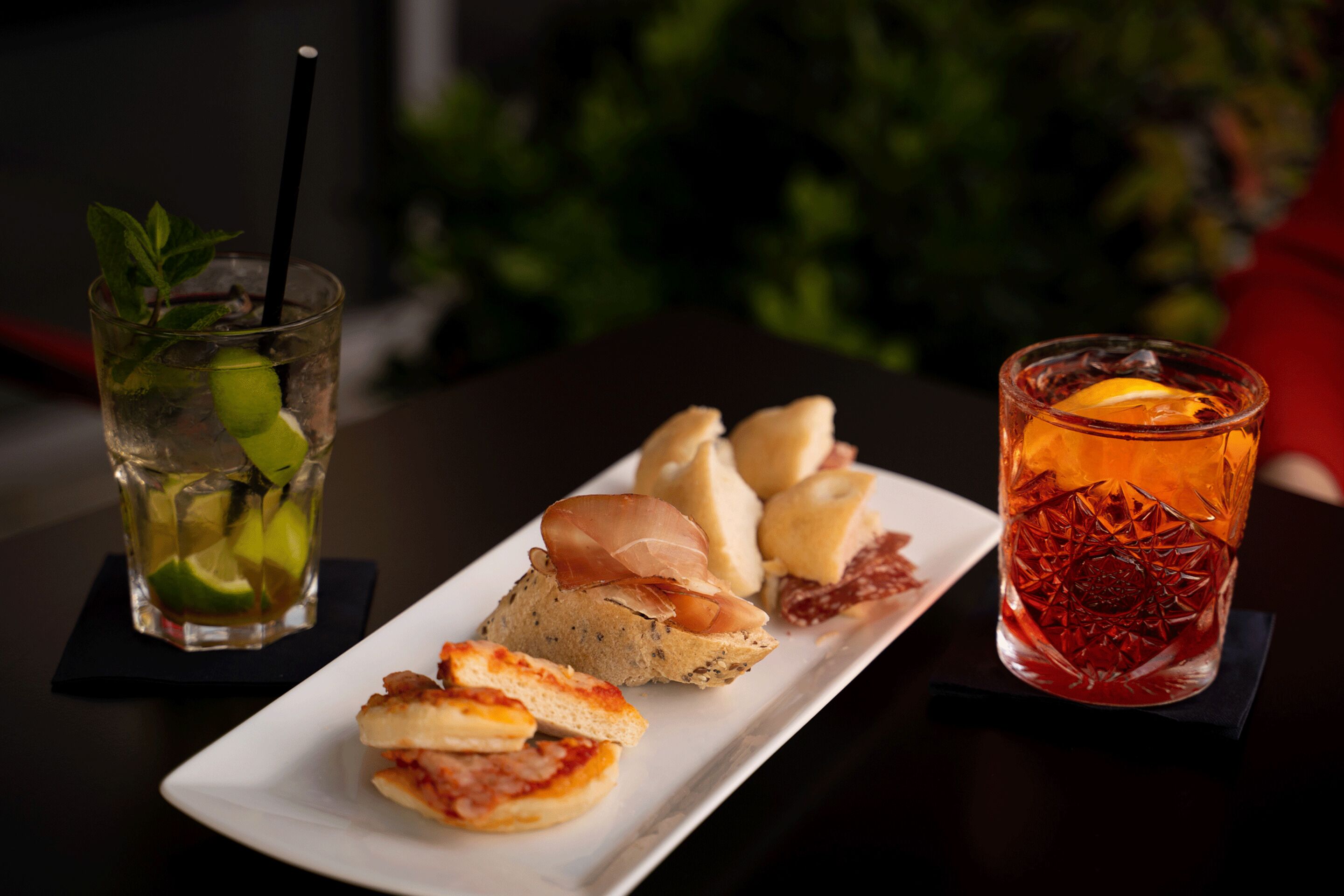 A table with a plate of food, a glass of iced tea with a lime, and a glass of red drink with an orange slice.