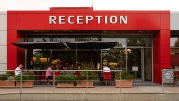 A reception area with a red facade, outdoor seating with red chairs, and a sign indicating the bar is open.