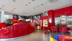 A red and white interior with a racing car display, red chairs, and colorful stools. - Hotel Maranello Village (Maranello)
