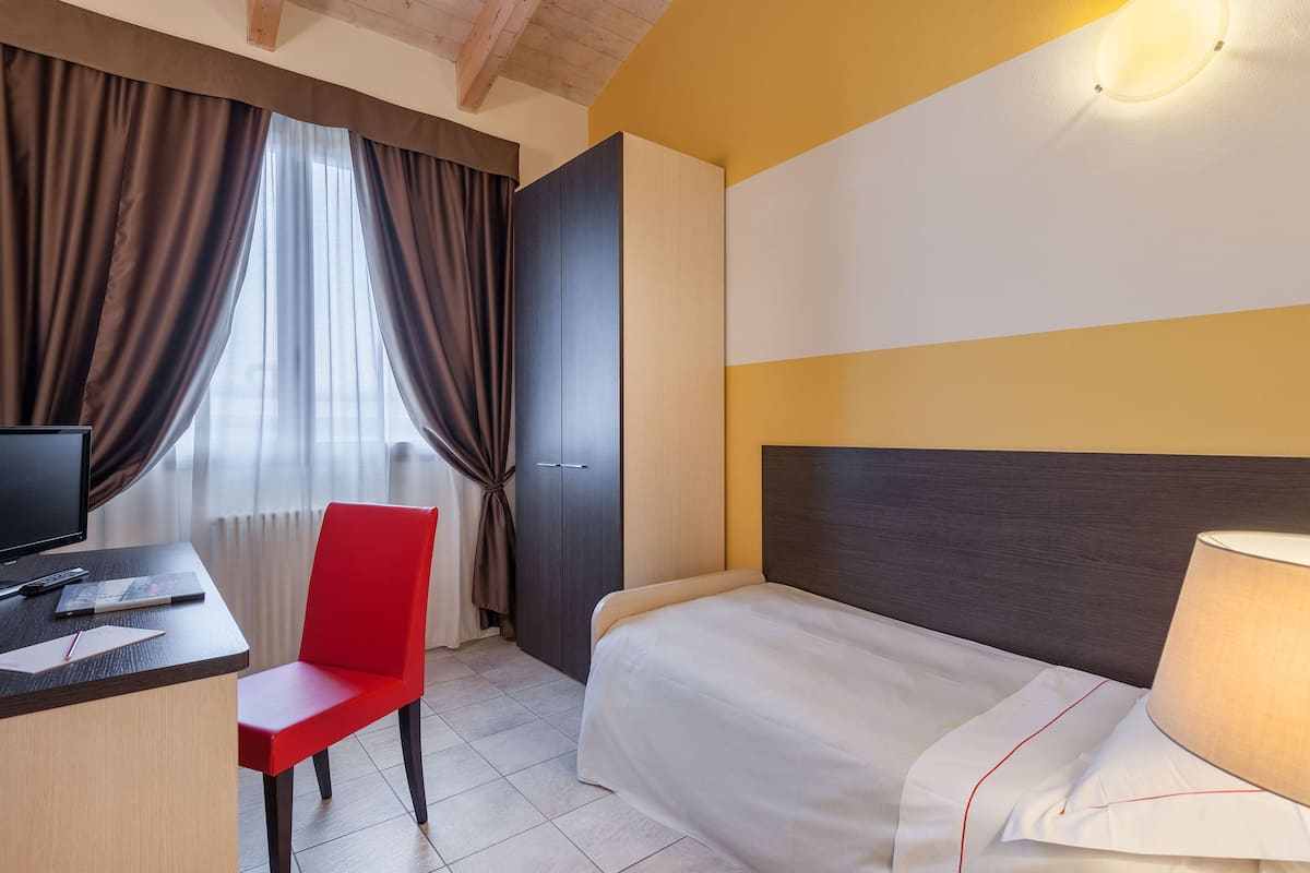 A hotel room with a bed, a desk with a computer, a chair, and a TV.