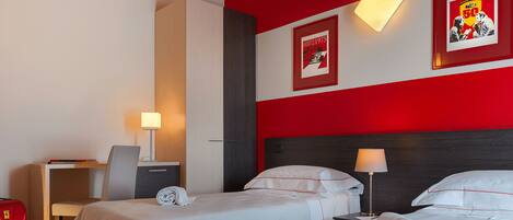 Een hotelkamer met twee bedden, een bureau, een stoel, een rode koffer en een muur met een lijst.