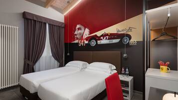 Quarto de hotel com uma cama, uma cadeira vermelha, uma pequena mesa com garrafas e uma parede com um carro e números.