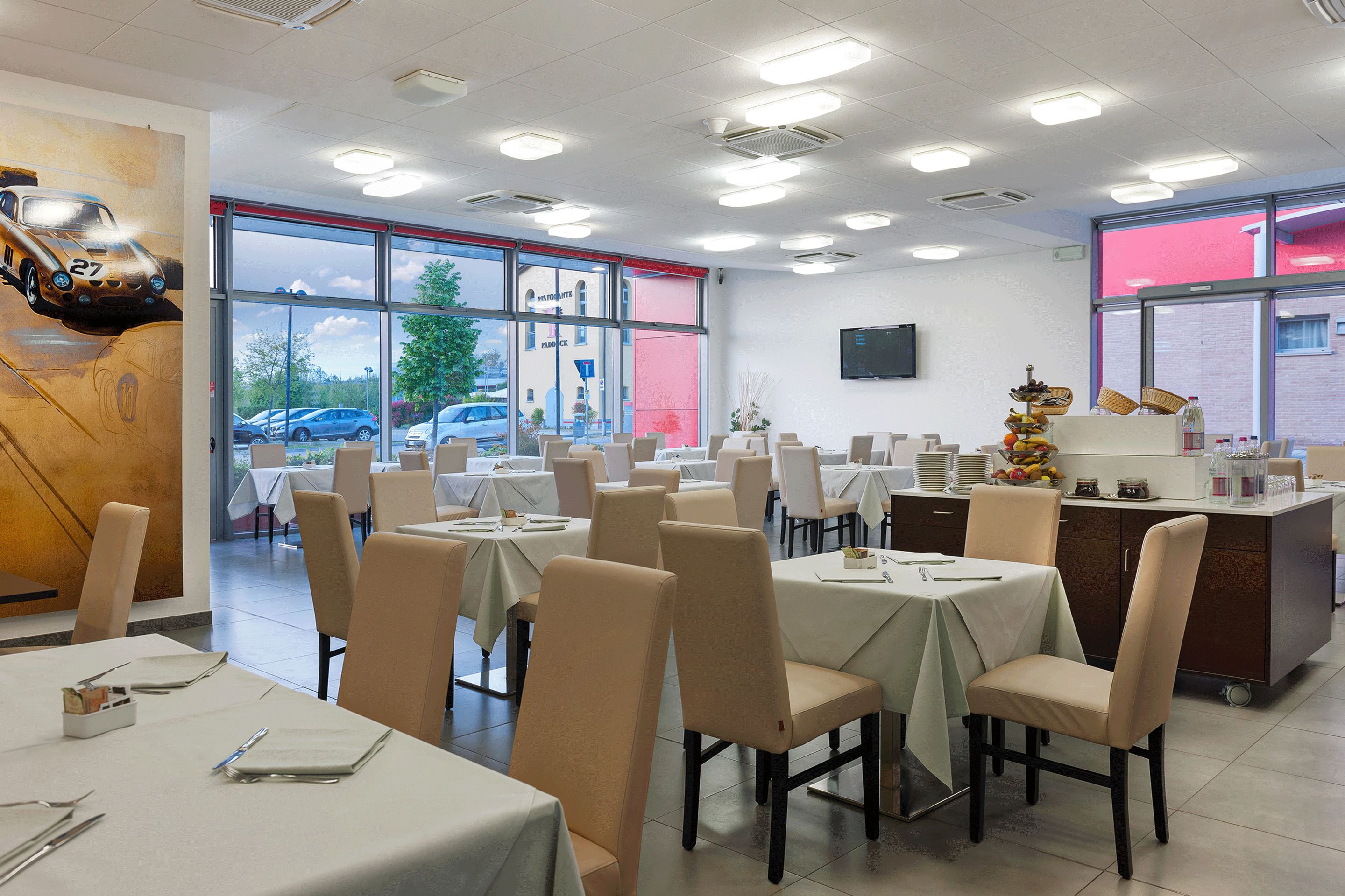 Un restaurante con varias mesas y sillas, ventanas amplias y una zona de cocina.