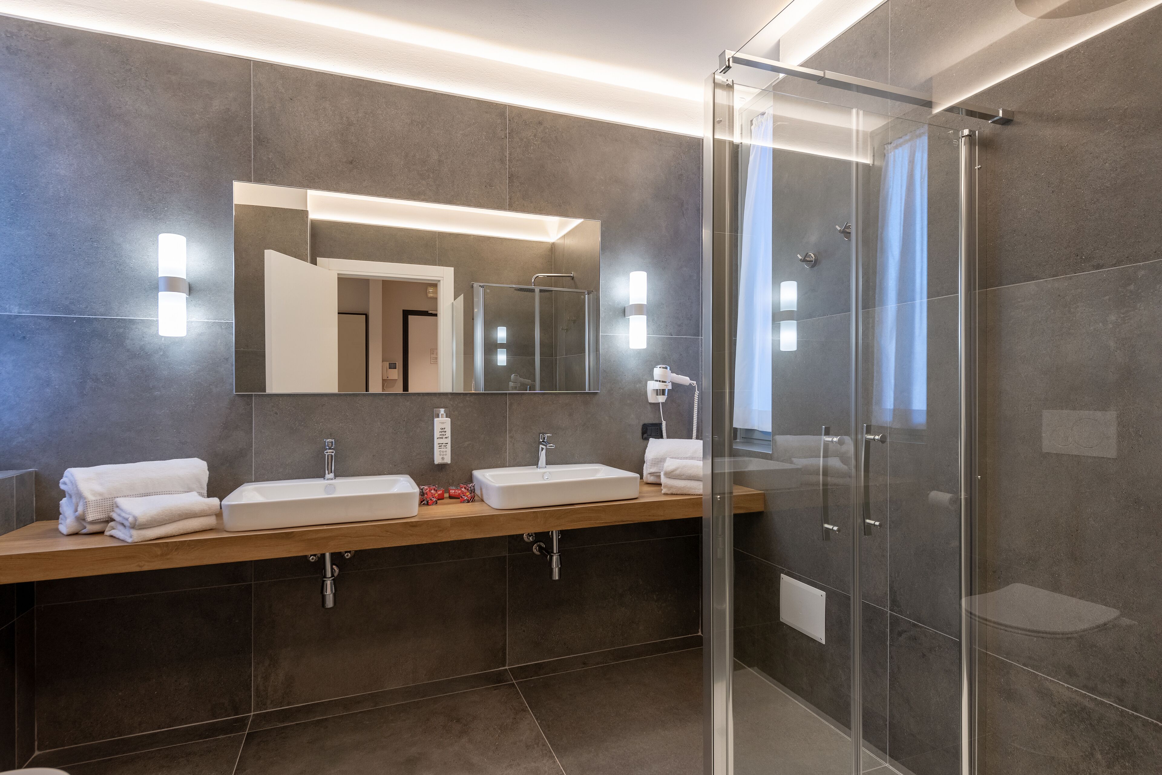 A modern bathroom with a large mirror, two sinks, a shower, and a glass-enclosed shower area.