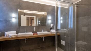A modern bathroom with a large mirror, two sinks, a shower, and a glass-enclosed shower area.