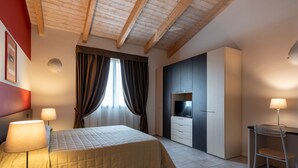 A bedroom with a bed, bedside lamps, a TV, and a wardrobe. - Hotel Maranello Village (Maranello)