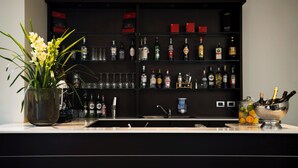 A bar area with shelves of liquor bottles, a sink, and a vase with flowers. - Hotel Maranello Village (Maranello)