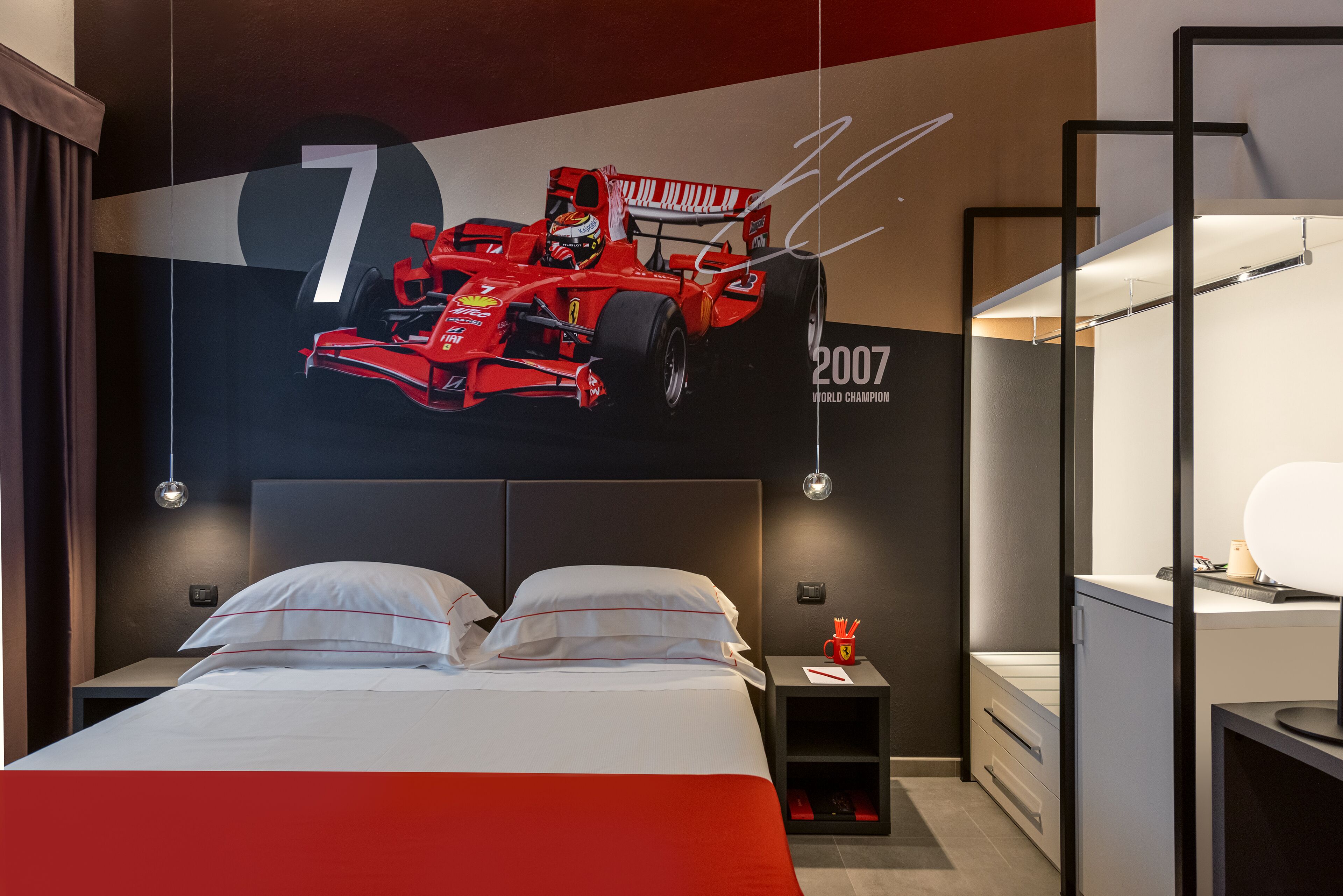 Een moderne hotelkamer met een groot bed, een nachtkastje, een bureau en een wanddecoratie van een rode raceauto.