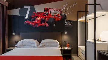 Een moderne hotelkamer met een groot bed, een nachtkastje, een bureau en een wanddecoratie van een rode raceauto.