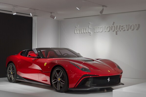 A red sports car in a showroom with a minimalist design and a large wall with text. - Hotel Maranello Village (Maranello)
