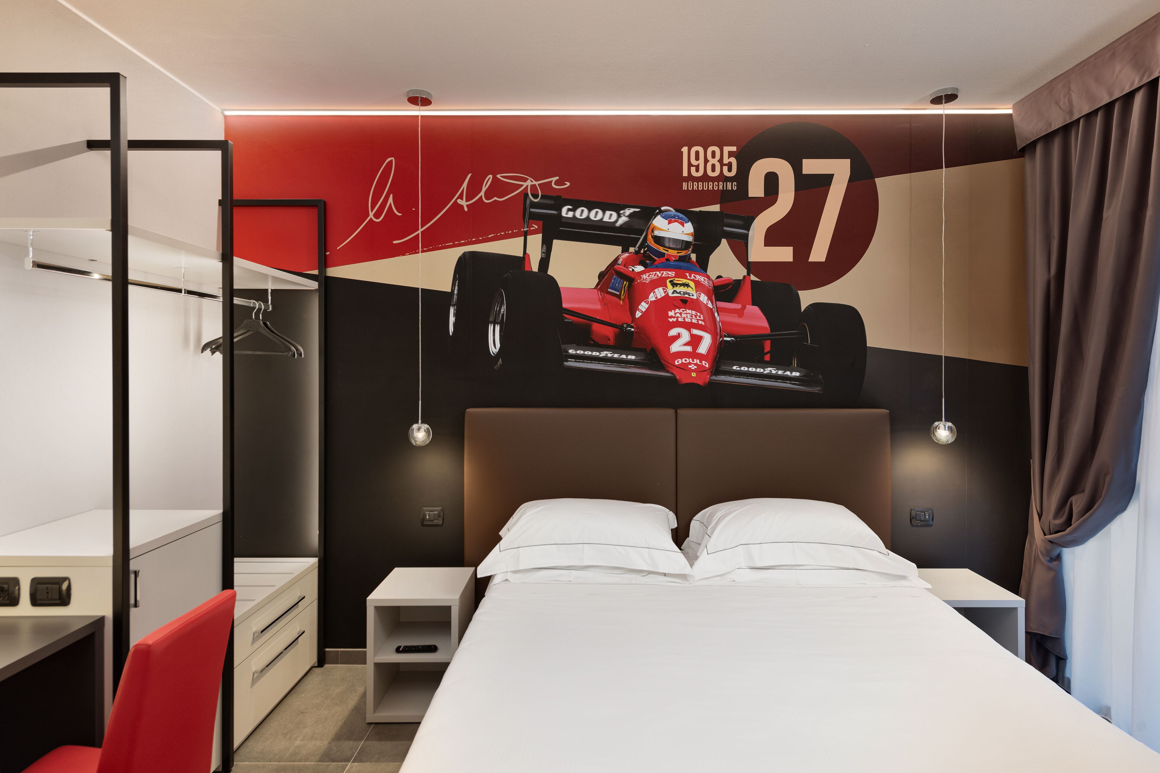 A hotel room with a bed, a desk, a chair, a wardrobe, and a wall with a racing car mural.