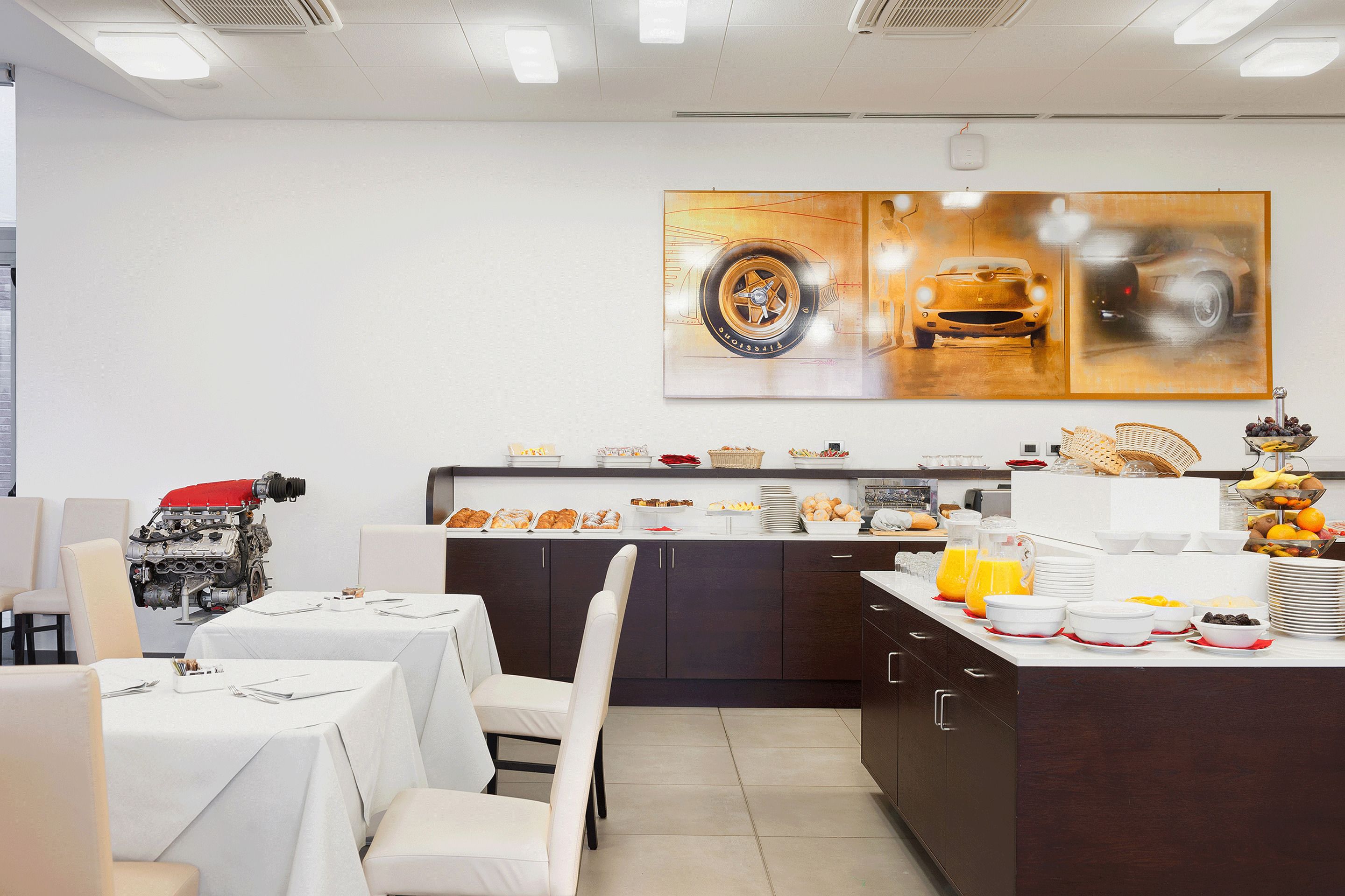 Een moderne keuken met een eethoek, met een groot schilderij van een auto, een koffiehoek en diverse ontbijtartikelen.