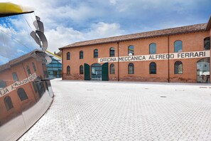 A building with the sign "OFFICINA MECCANICA ALFREDO FERRARI" and a large, curved structure to the left. - Hotel Maranello Village (Maranello)
