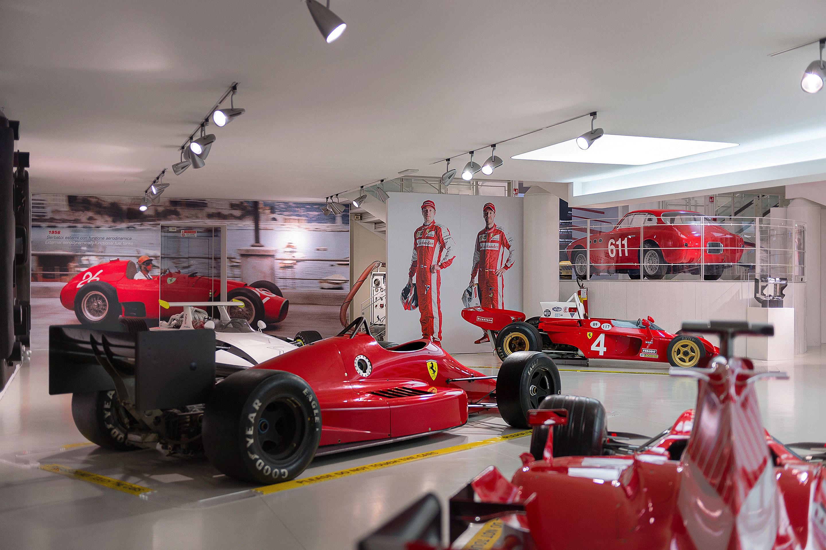 A museum exhibit with vintage racing cars, including a Ferrari and a Porsche, displayed in a modern, well-lit interior with glass display cases.