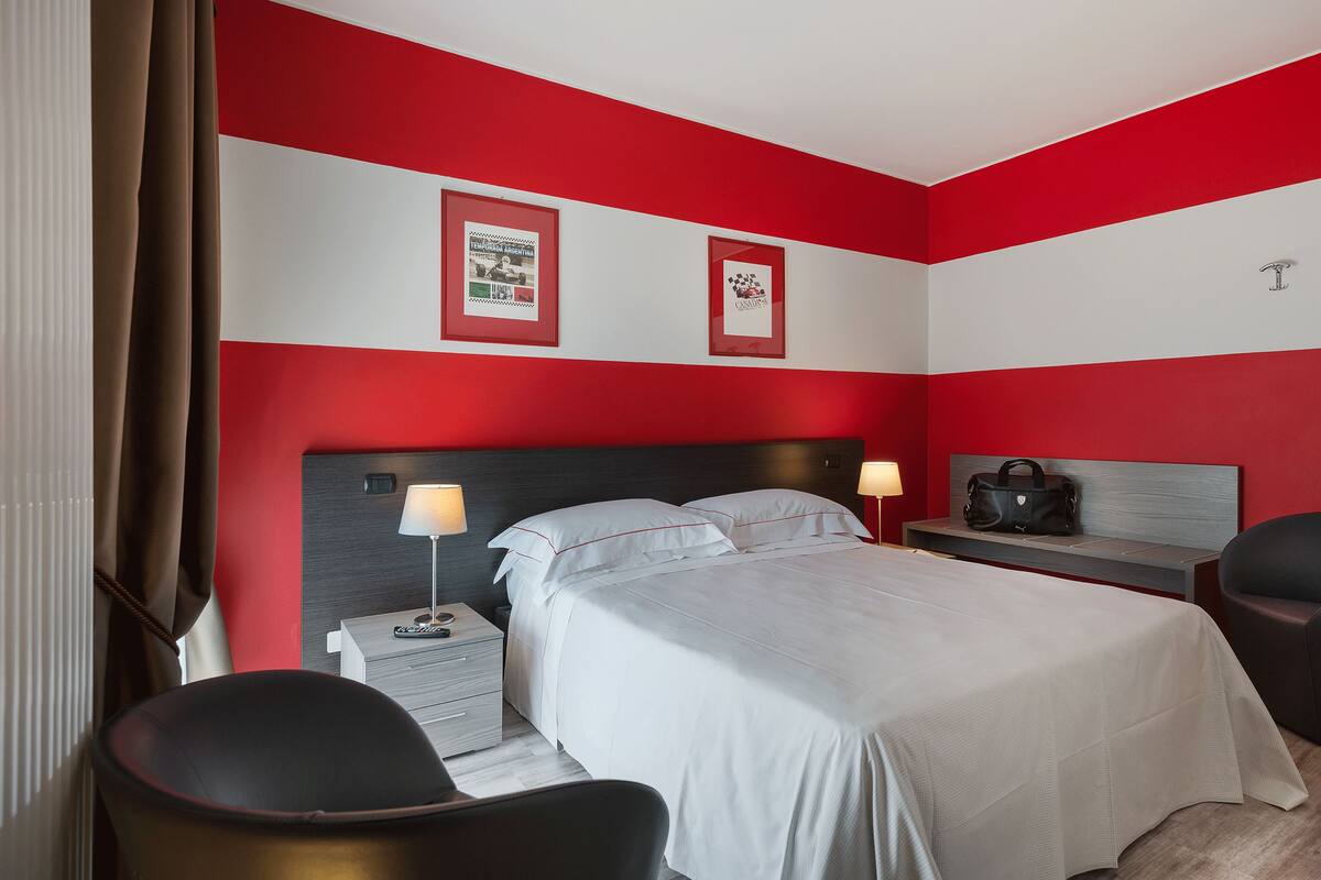 A hotel room with a bed, bedside tables, a chair, and a nightstand with a lamp.