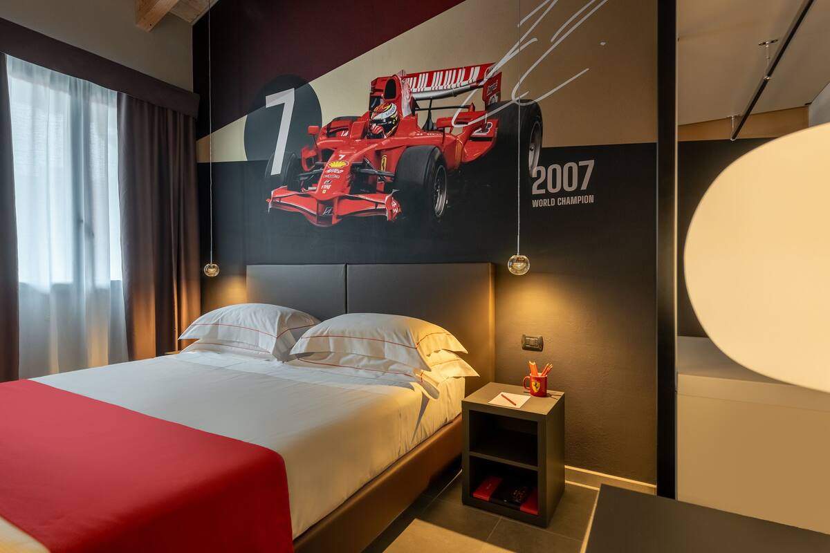 A modern hotel room with a large bed, a nightstand, and a wall mural of a racing car.