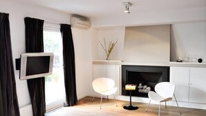 A modern living room with a fireplace, a mounted TV, and two white chairs.
