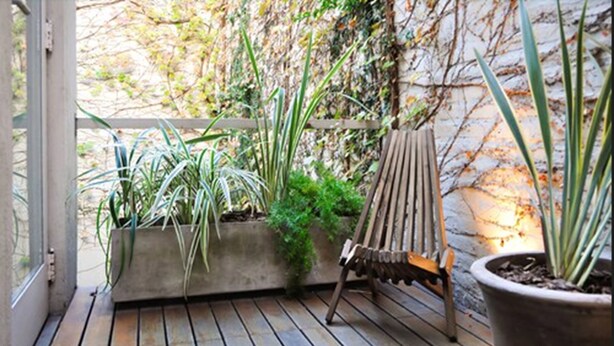 A wooden deck with potted plants and a wooden chair.