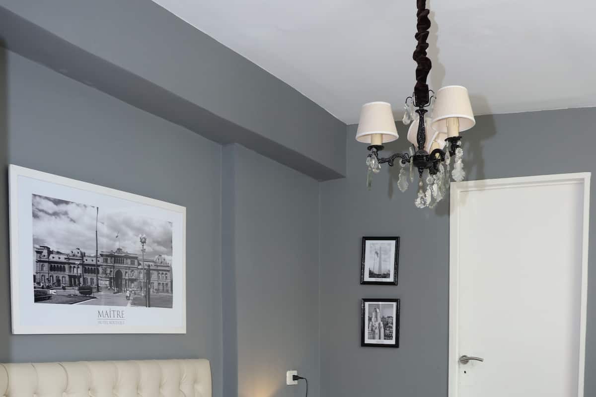 Ein ordentlich bezogenes Bett mit einer karottenförmigen Kopfteil, ein Nachttisch mit einer Lampe und gerahmte Bilder an der Wand.