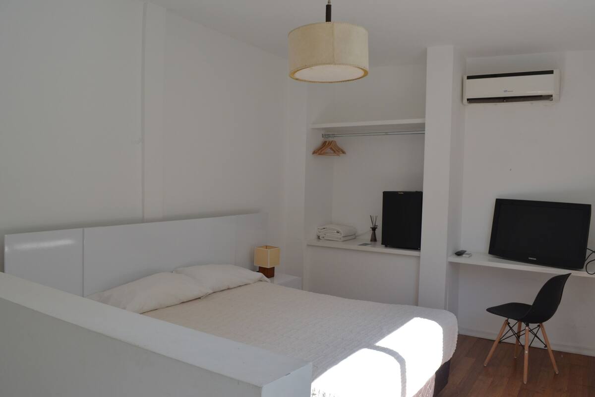Ein Schlafzimmer mit Bett, Schreibtisch, Stuhl, Fernseher, Klimaanlage und einer Pendelleuchte.