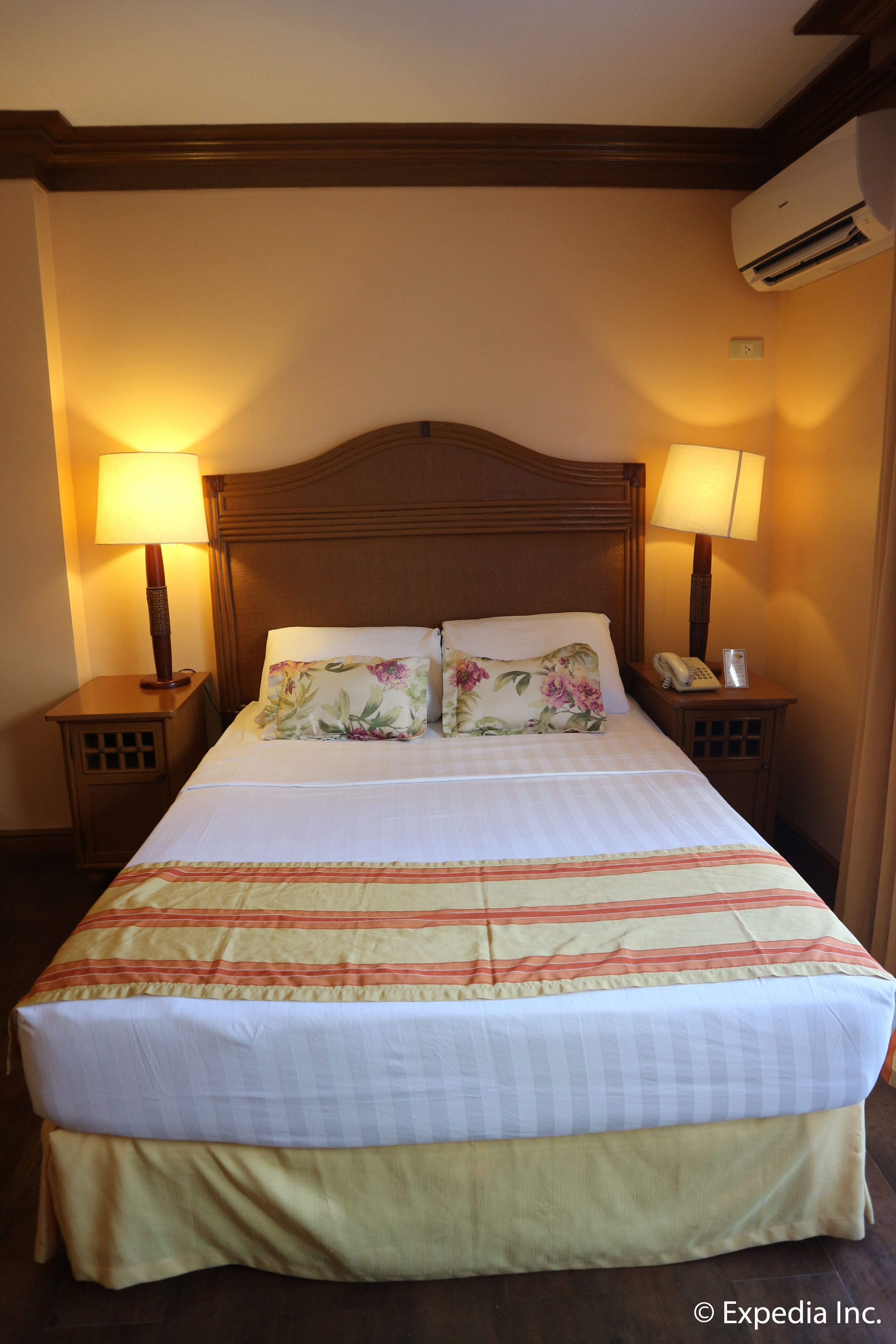 Habitación de hotel con una cama grande, dos lámparas de noche, un teléfono y un equipo de aire acondicionado.