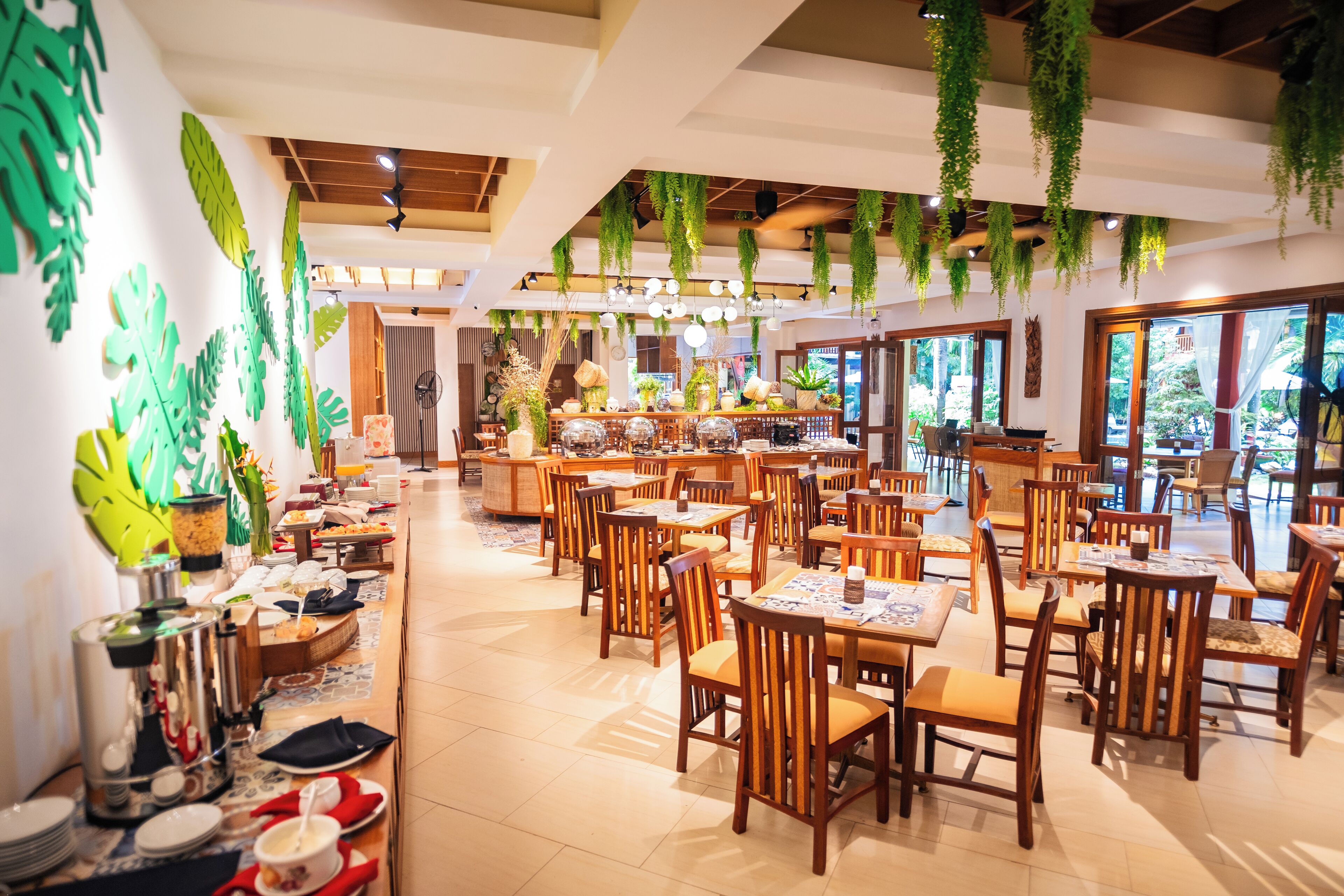 Un restaurante espacioso con mesas y sillas de madera, plantas colgantes y una zona de bufé.