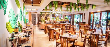 Un restaurante espacioso con mesas y sillas de madera, plantas colgantes y una zona de bufé.