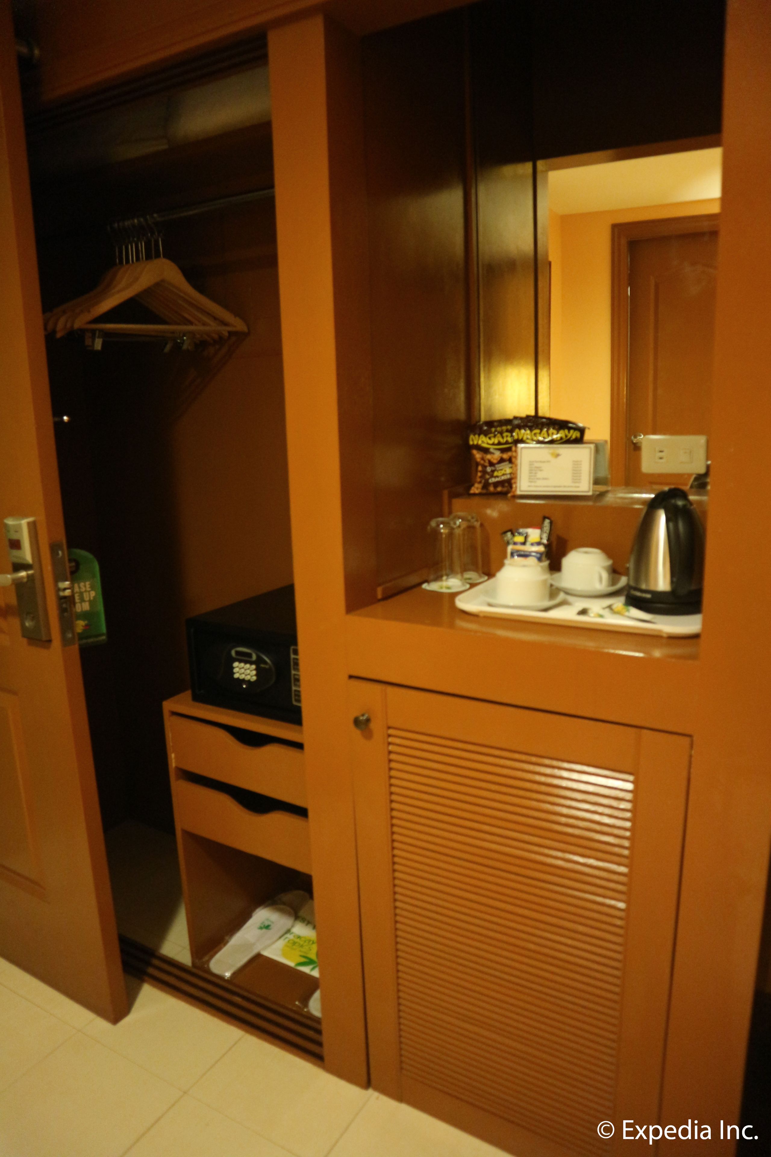 Habitación de hotel con armario de madera, minibar, microondas, tetera y una mesita con tazas y bandeja.
