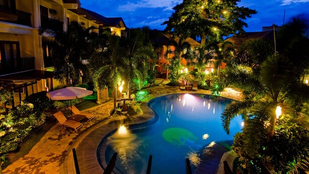 A pool area with lounge chairs and umbrellas, surrounded by buildings and greenery. - Boracay Tropics Resort Hotel (Boracay Island)