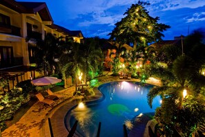 A pool area with lounge chairs and umbrellas, surrounded by buildings and greenery.