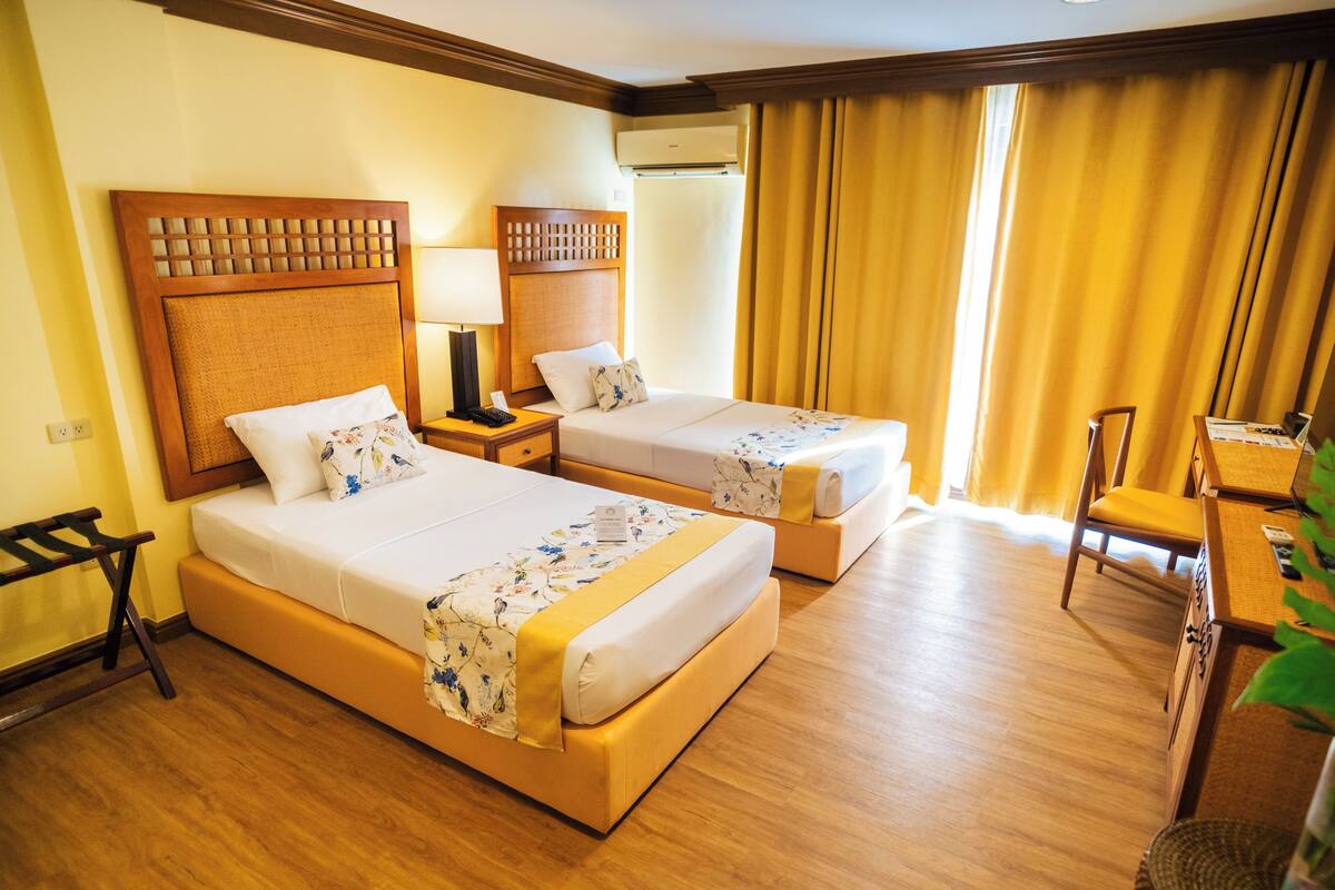 Una habitación de hotel con dos camas, cabeceros de madera, un escritorio y una silla.