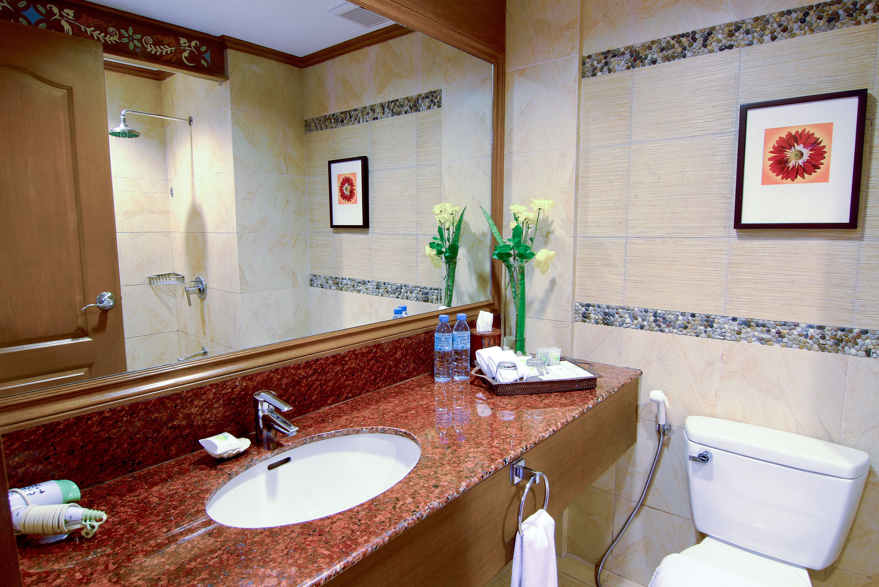 A bathroom with a marble sink, a toilet, a shower, and framed artwork on the wall.