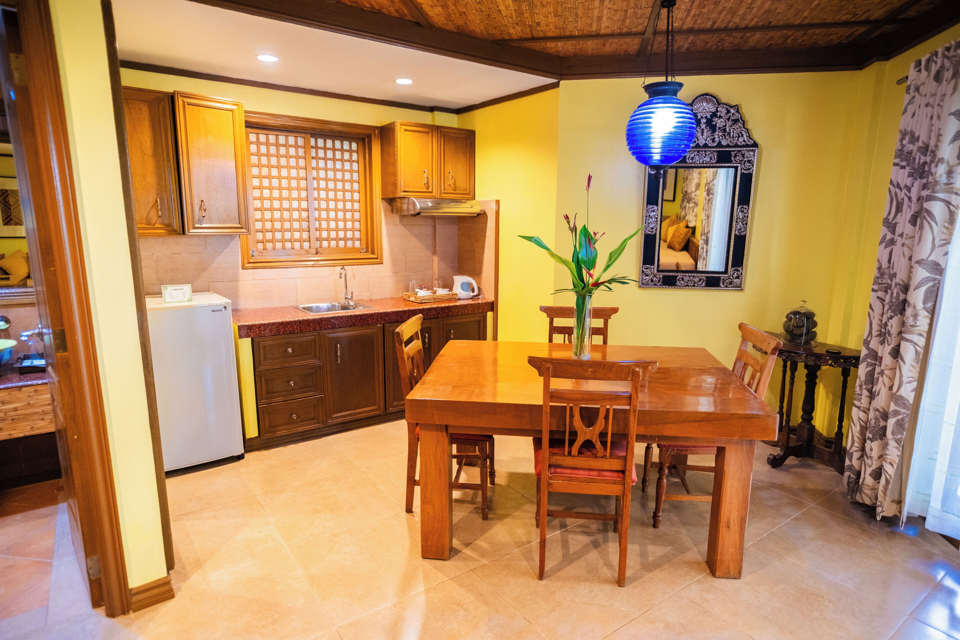 A dining area with a wooden table and chairs, a refrigerator, wooden cabinets, and a decorative mirror.