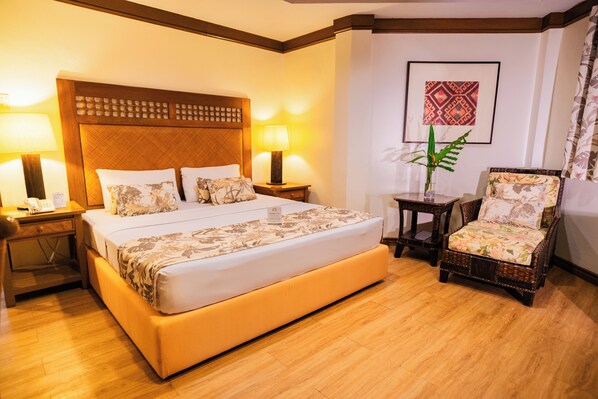 A hotel room with a large bed, two bedside tables with lamps, a chair, and a framed picture on the wall.